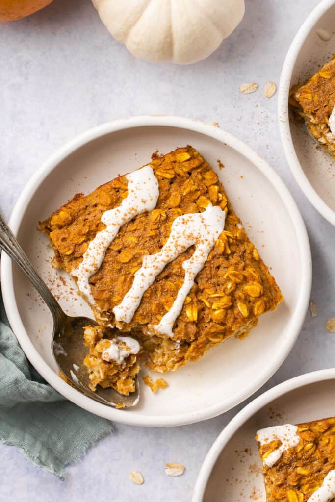 Healthy pumpkin oatmeal bake drizzled with vanilla maple cream cheese glaze served on a small plate with a spoon.