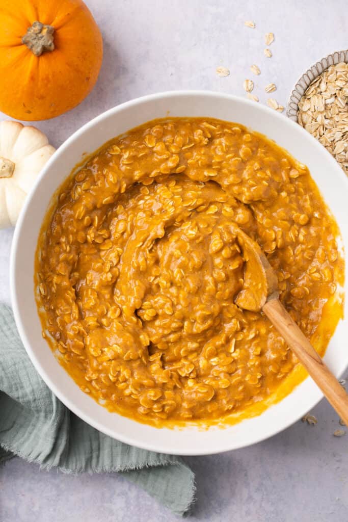 All ingredients for healthy pumpkin oatmeal bake mixed together in a mixing bowl with a wooden spoon.