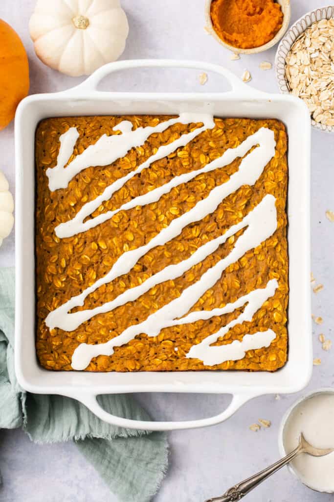 Healthy pumpkin oatmeal bake in a square baking drizzled with glaze.