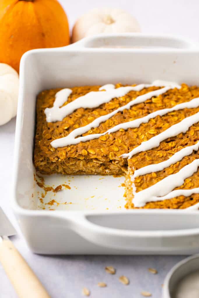 Healthy pumpkin oatmeal bake drizzled with glaze in a baking dish with a square serving missing. 