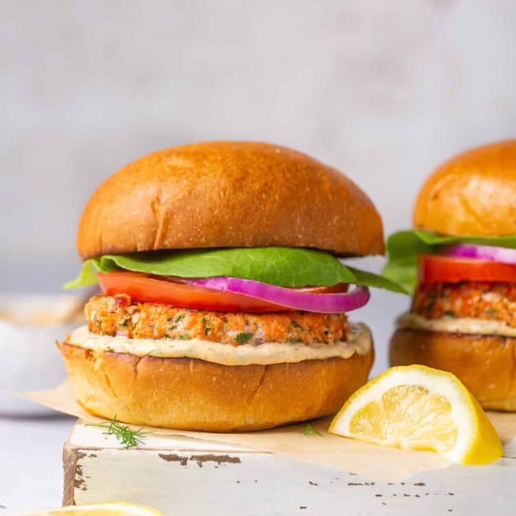 Healthy salmon burger with veggie toppings and creamy lemon dill sauce on a bun.
