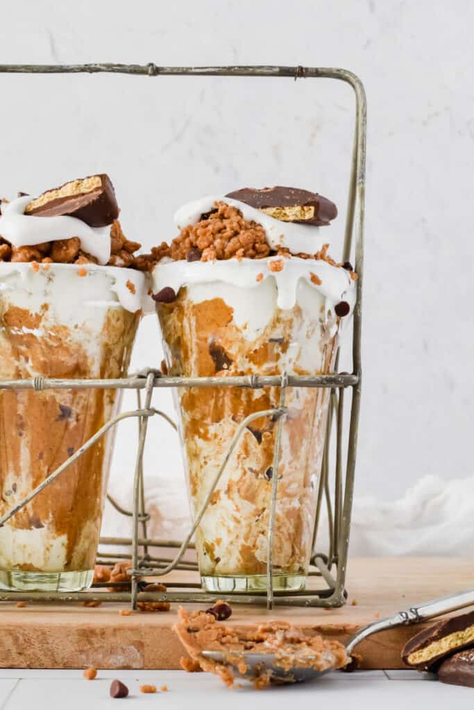 High protein cookie dough on top of milkshakes in three tall glasses with spoons.
