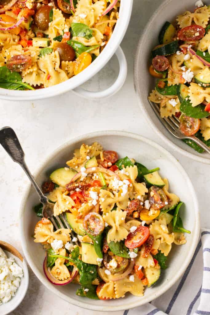 Healthy tuscan sun dried tomato pasta salad in a bowl with a fork sprinkled with feta cheese.