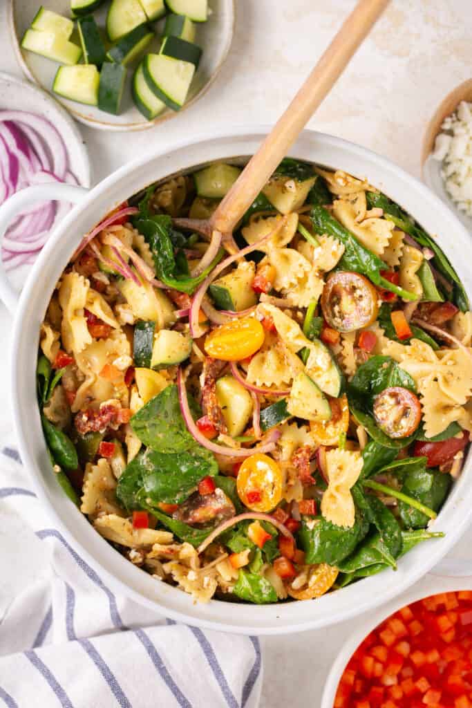 sun dried tuscan pasta salad in a large bowl with a wooden spoon.