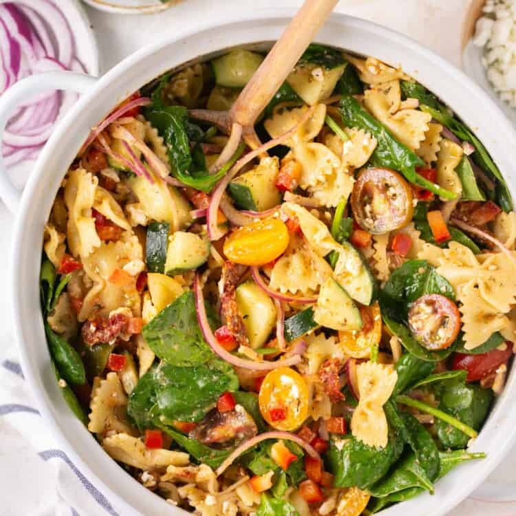 sun dried tuscan pasta salad in a large bowl with a wooden spoon.