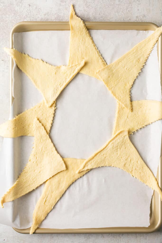 Crescent roll triangles laid out in a ring on a baking sheet with parchment paper.