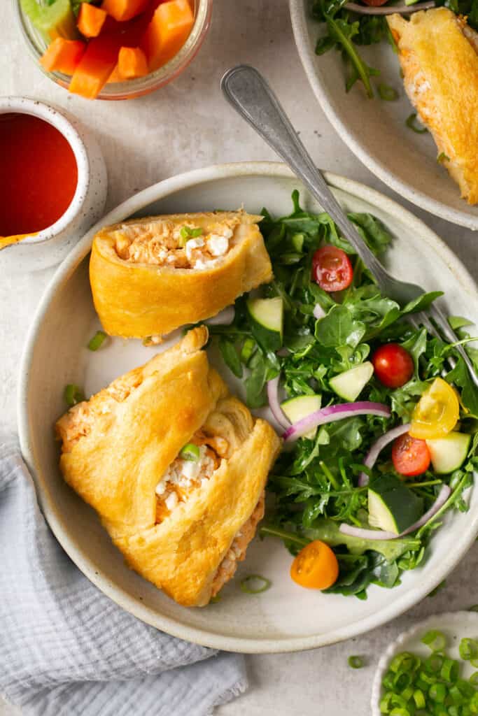 Buffalo chicken crescent ring sliced on a two plates both with a side salad.