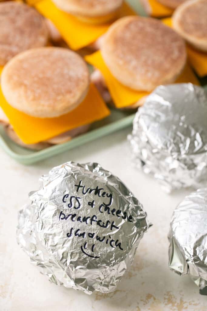 Breakfast sandwiches wrapped in foil and some on unwrapped on a tray.