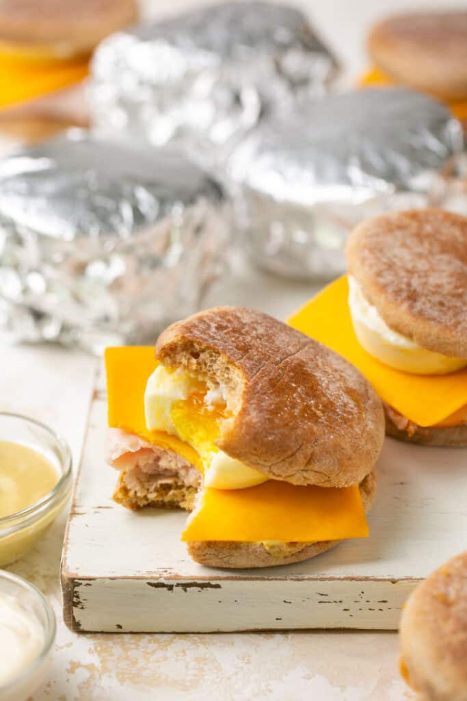 Meal prep breakfast sandwiches, one with a bite taken out of it and some wrapped with foil.