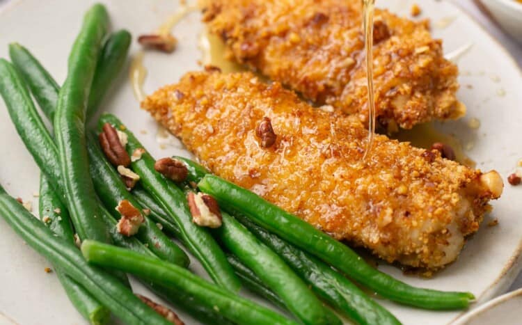 Pecan crusted chicken tenders drizzled with honey and served on plates with green beans.