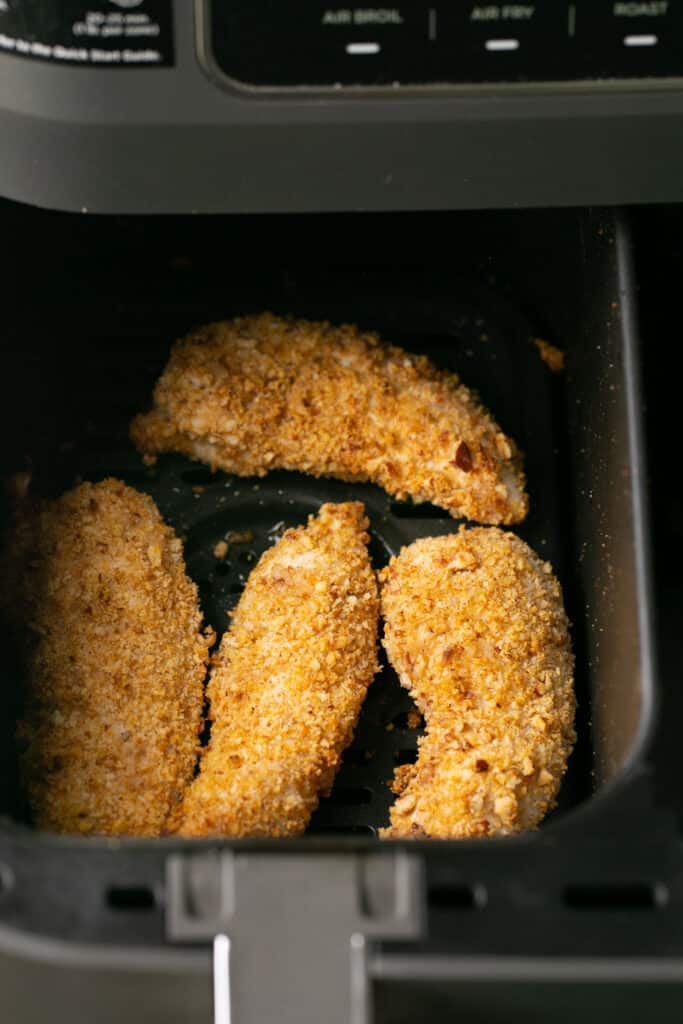 Pecan crusted chicken tenders in an air fryer basket after being cooked.