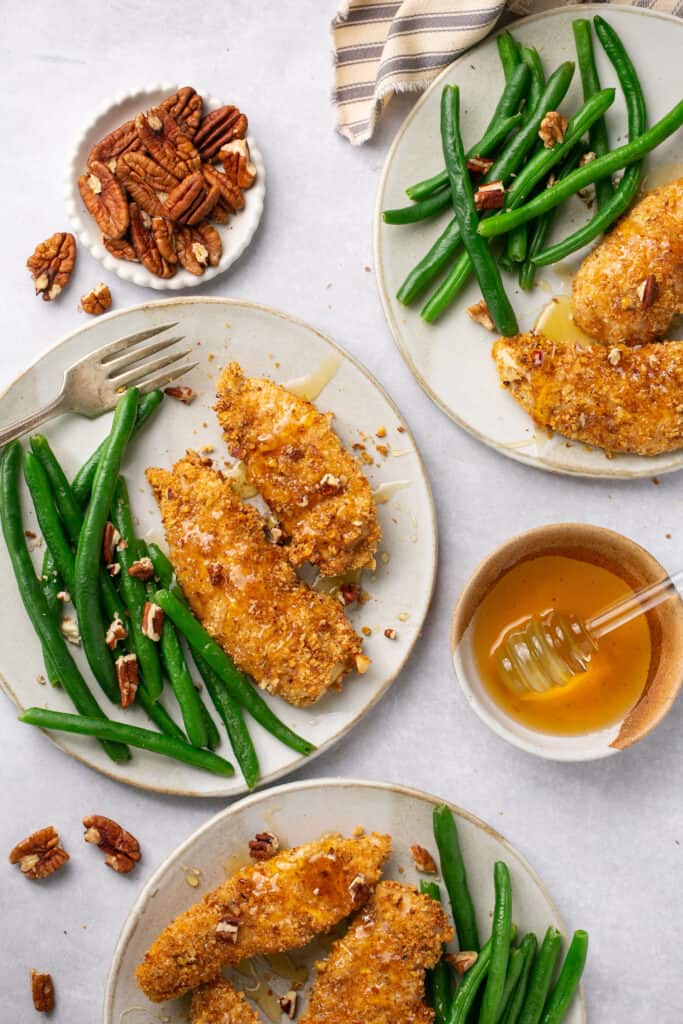 Several servings of pecan crusted chicken tenders drizzled with honey and served on plates with green beans