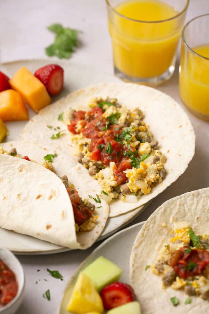 High protein breakfast tacos open faced on a plate with fruit.