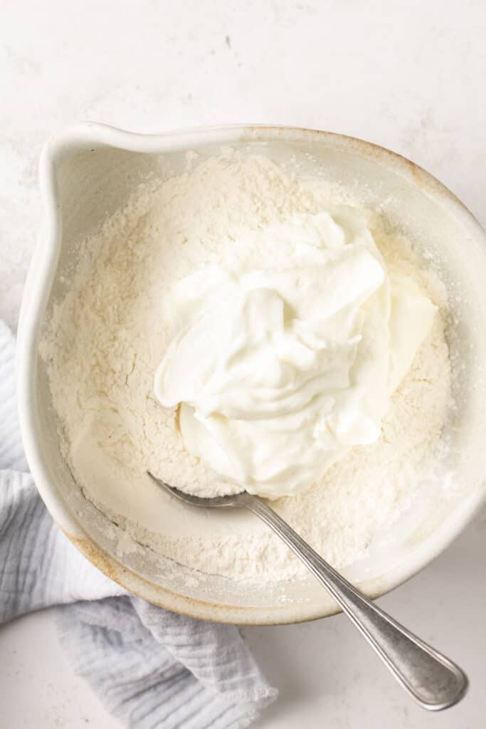 Flour and yogurt in a mixing bowl with a spoon before being mixed together.