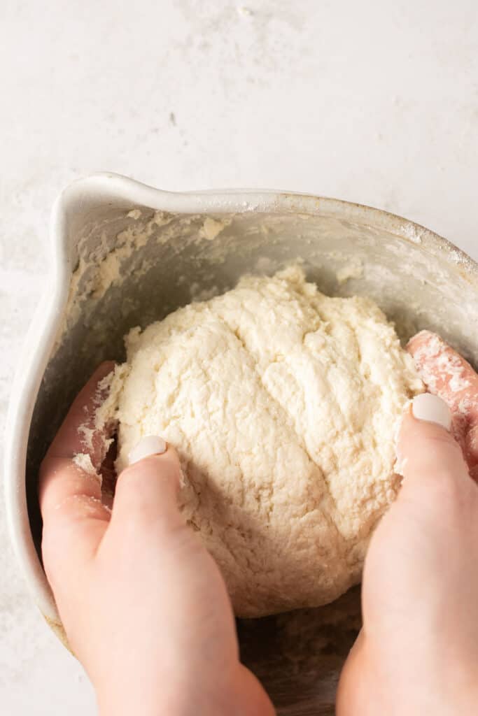 Hand holding a bowl of of dough in a mixing bowl.
