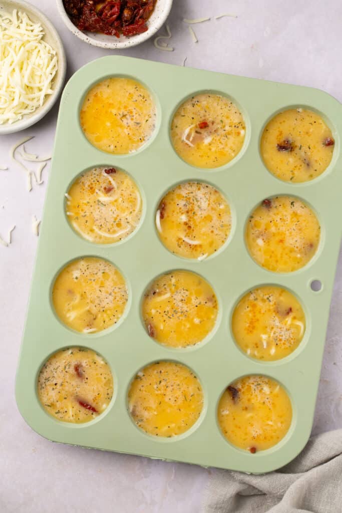 Sun dried tomato egg bites in a muffin pan before being baked.