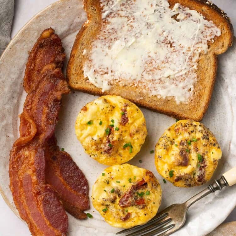 Sun dried tomatoe egg bites, bacon, and toast with butter on a plate.