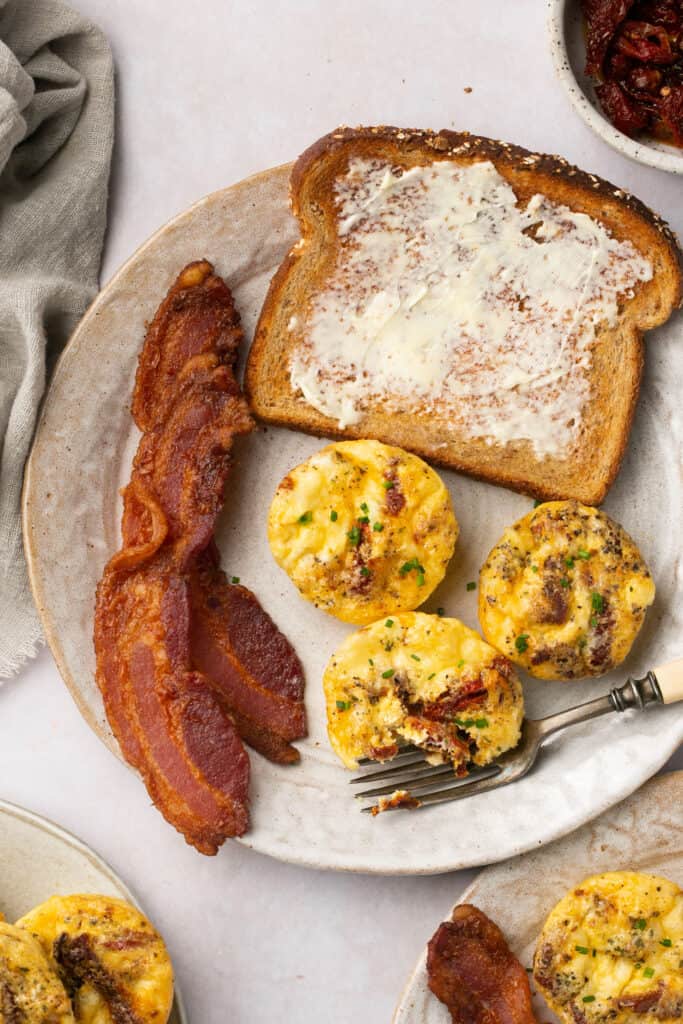 Sun dried tomato egg bites, bacon,and toast with butter on a plate.