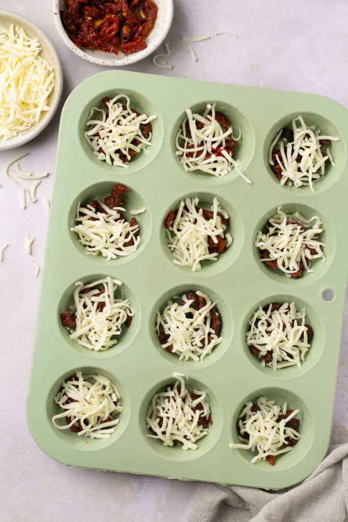 Sun dried tomatoes and  shredded cheese in a muffin pan.