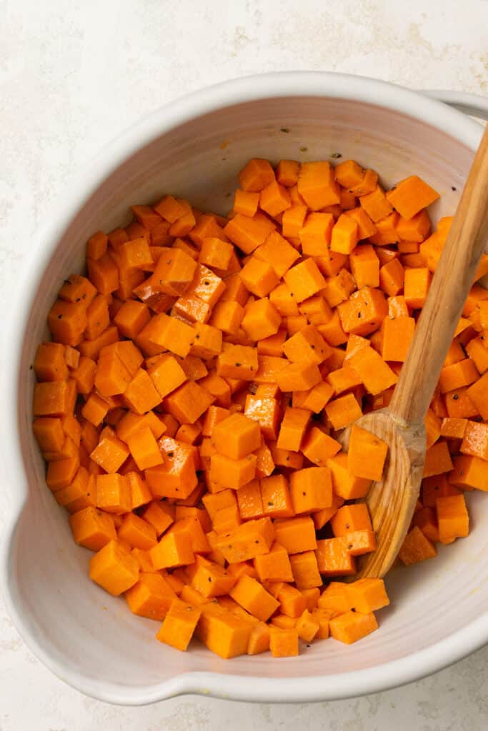 Cubed sweet potatoes in a mixing bowl with a wooden spoon.