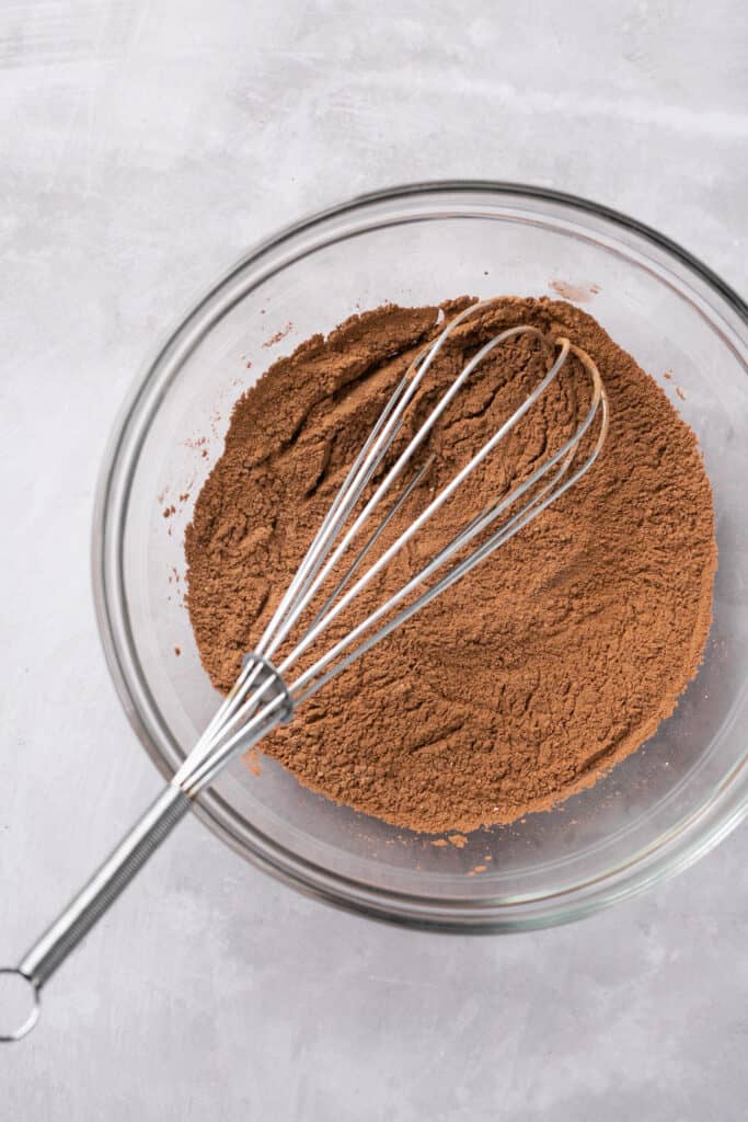 Cocoa powder and baking powder in a glass bowl with a whisk.