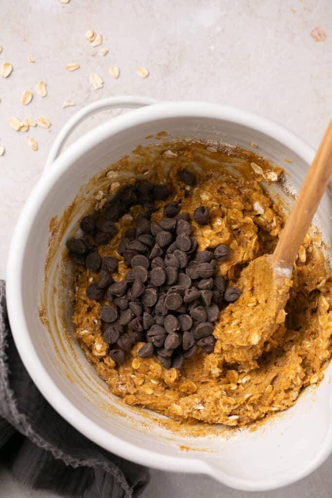 Chocolate chips added to the batter in a mixing bowl with a wooden spoon.