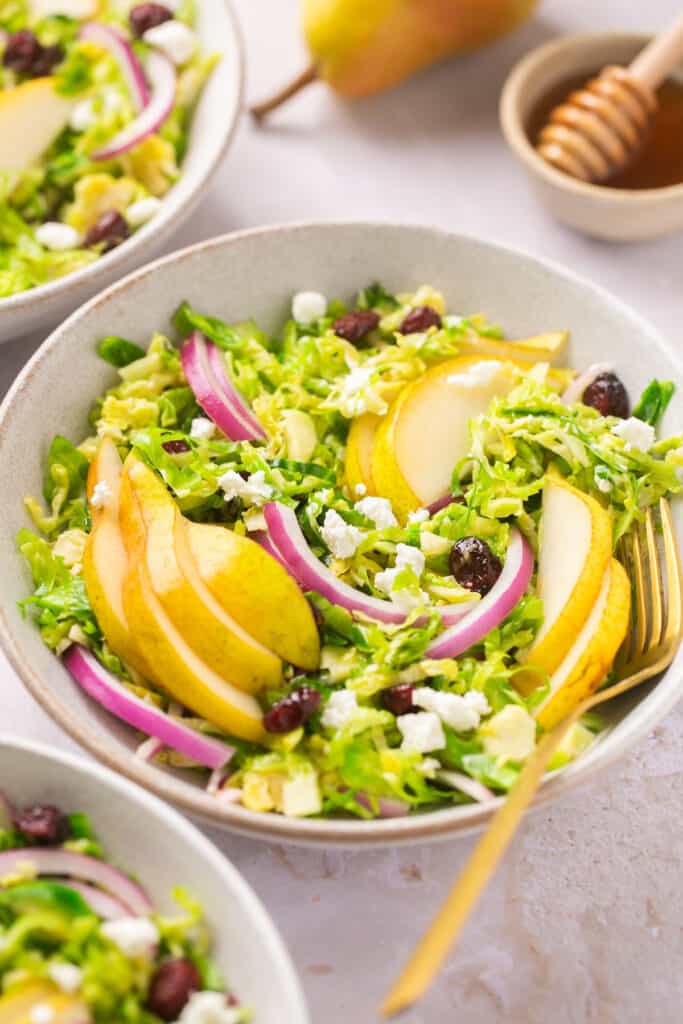 Several bowls of shaved brussel sprout salad with dijon vinaigrette topped with sliced apples, red onion, and crumbled cheese.
