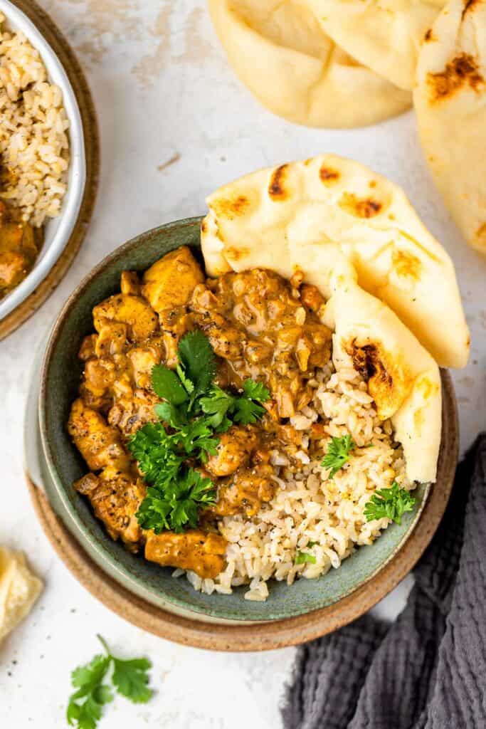 Healthy chicken curry served in bowl with rice and pita bread, garnished with cilantro
