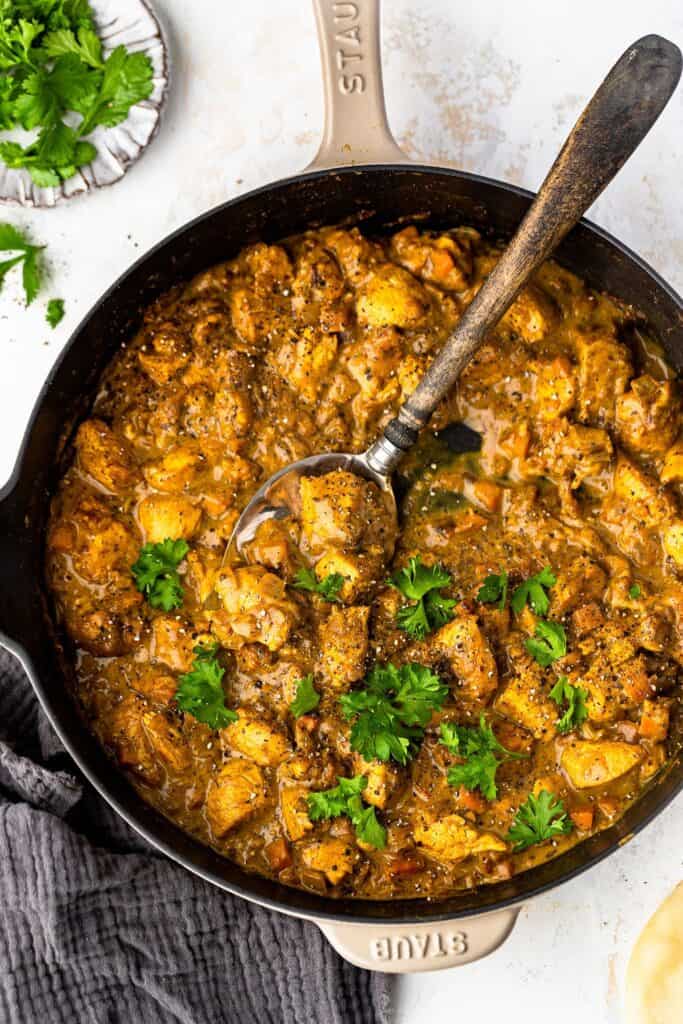 Healthy chicken curry in a skillet with a spoon topped with cilantro