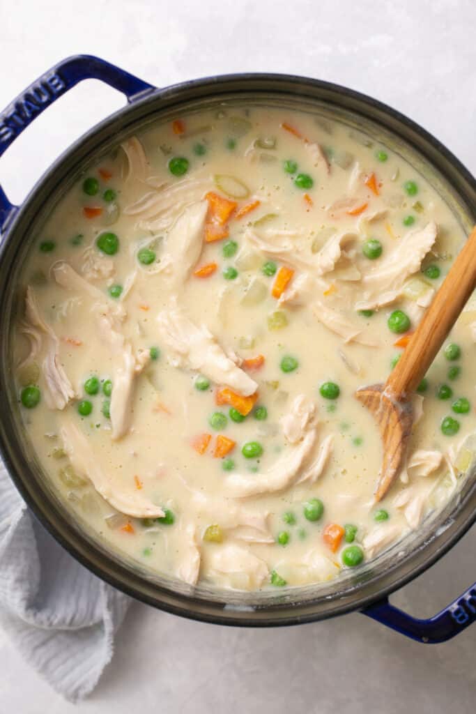 Creamy healthy chicken pot pie soup in a pot with a wooden spoon