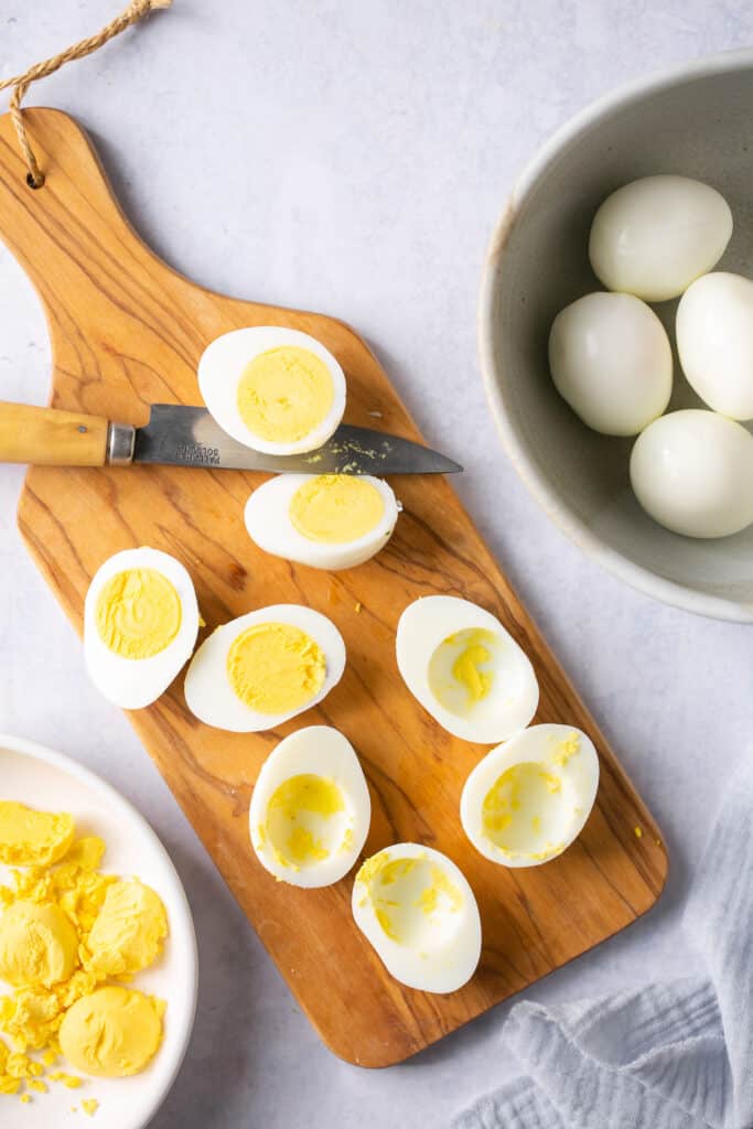 Hard boiled eggs cut in half on a cutting board, some with the yolk taken out.