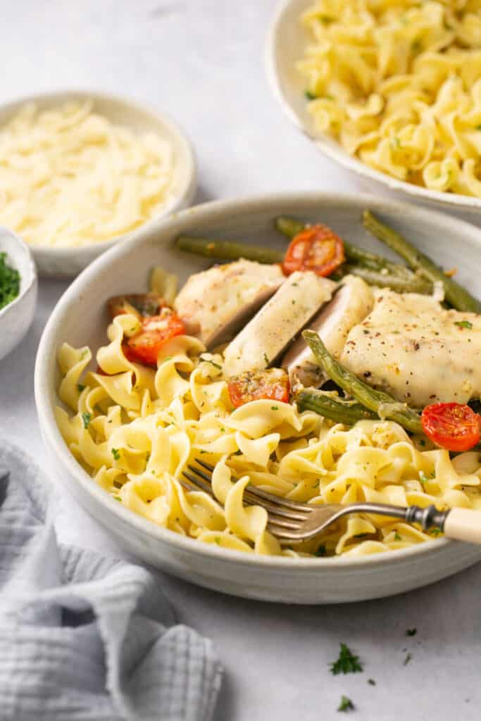 Buttery noodles in a bowl with a spoon topped with chicken, green beans, and tomatoes