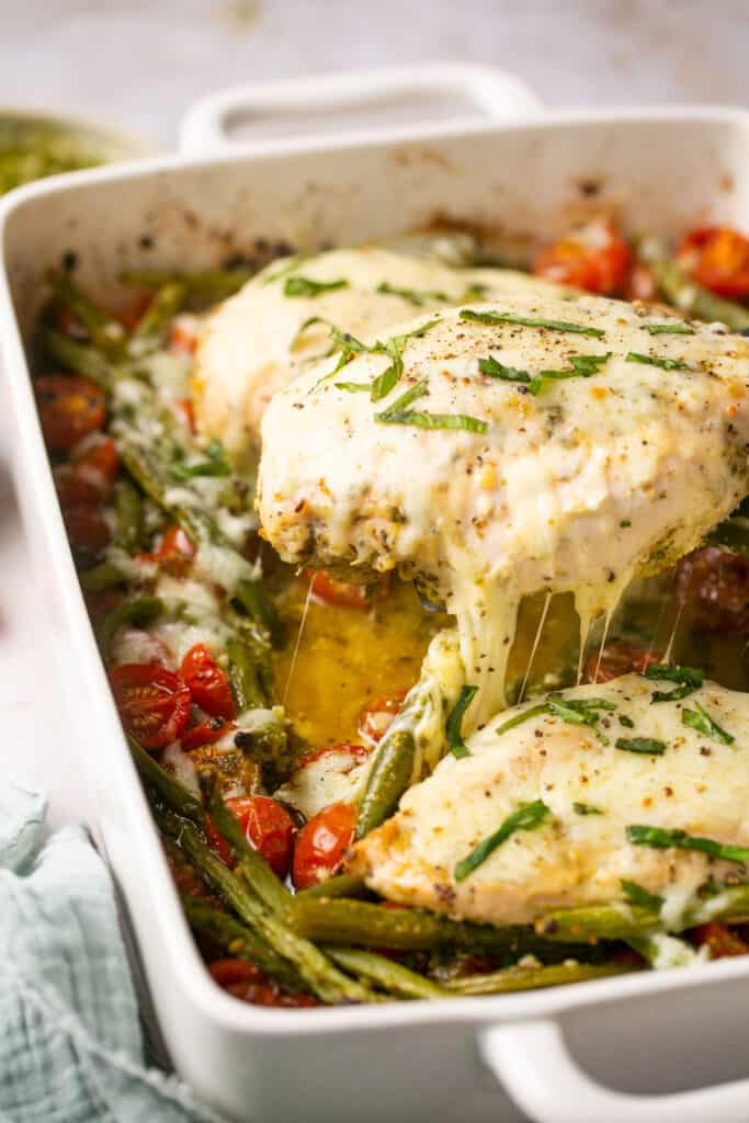 Baked chicken pesto topped with melty cheese in a baking dish