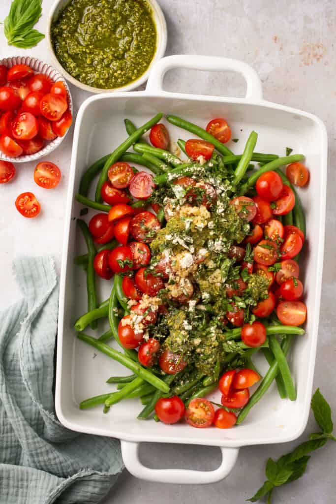 Tomatoes and green beans topped with pesto sauce in a baking dish.