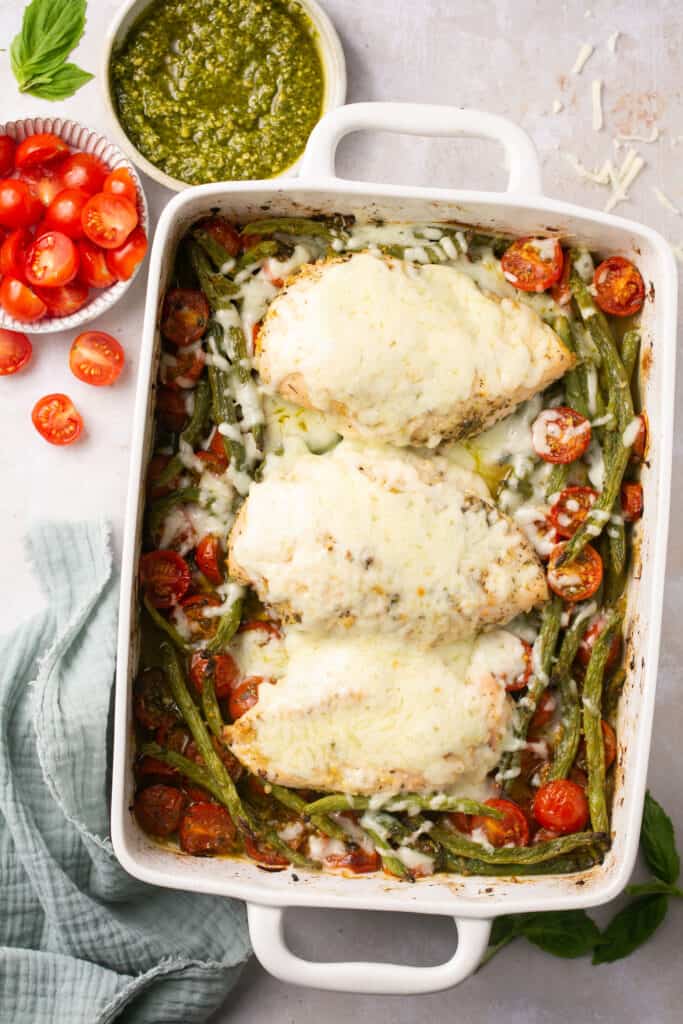 Baked pesto chicken topped with melted mozzarella cheese in a baking dish.