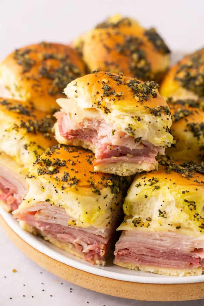 Healthy ham and cheese sliders stacked on a plate, one with a bite taken out of it.
