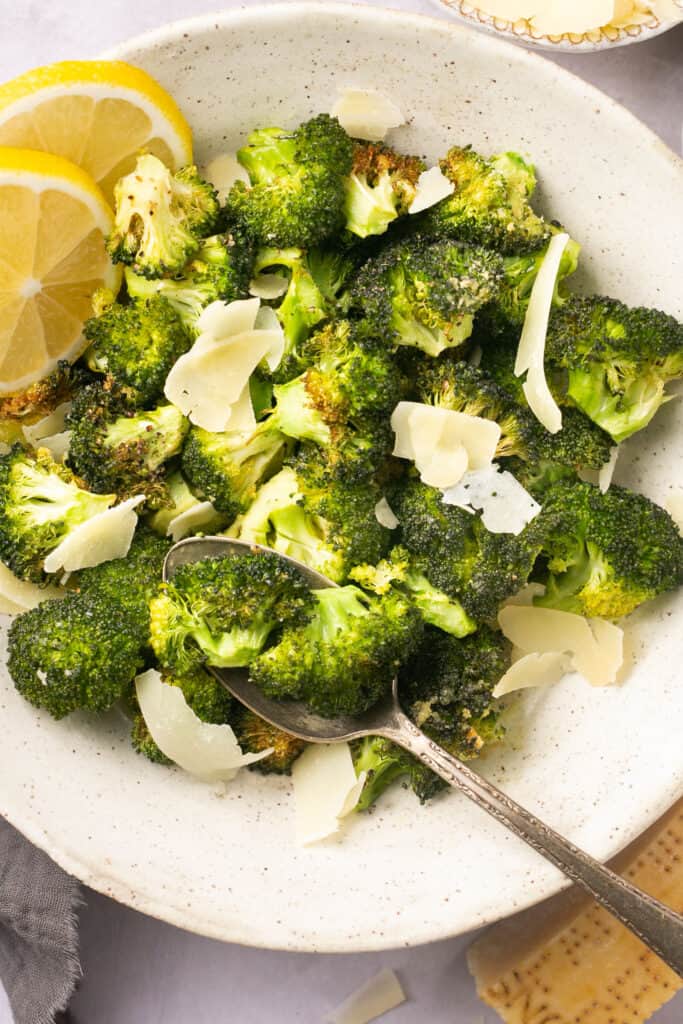 Air fryer broccoli in bowl with a spoon garnished with lemon and spinkled with parmesan cheese