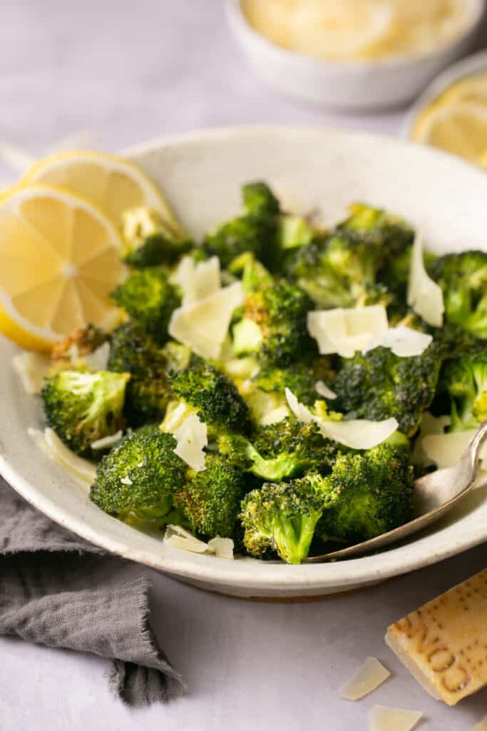 Air fryer broccoli in bowl garnished with lemon and spinkled with parmesan cheese