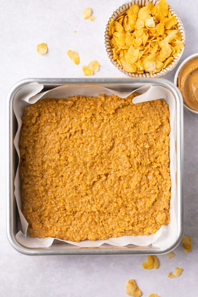 Peanut butter cornflake bar in a square baking dish with parchment paper.