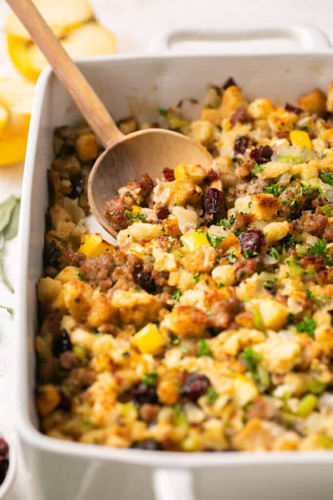 Sausage and sage stuffing with apples and cranberries in a baking dish with a serving spoon
