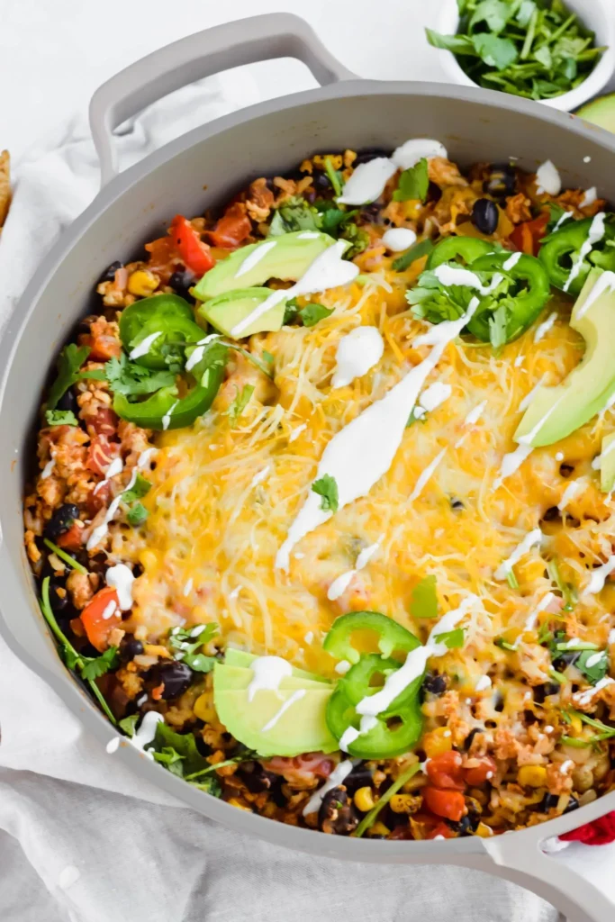 Cheesy mexican chikcen in a skillet topped with cheese, avocado, and jalapeño
