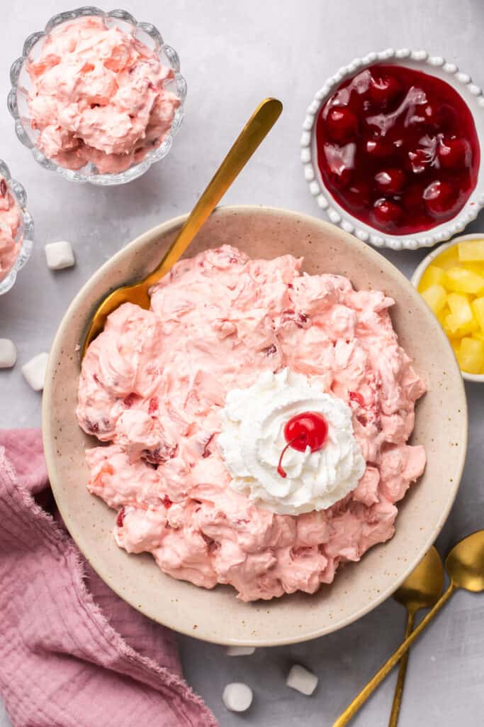 Cherry fluff recipe in a bowl topped with whipped cream and a cherry