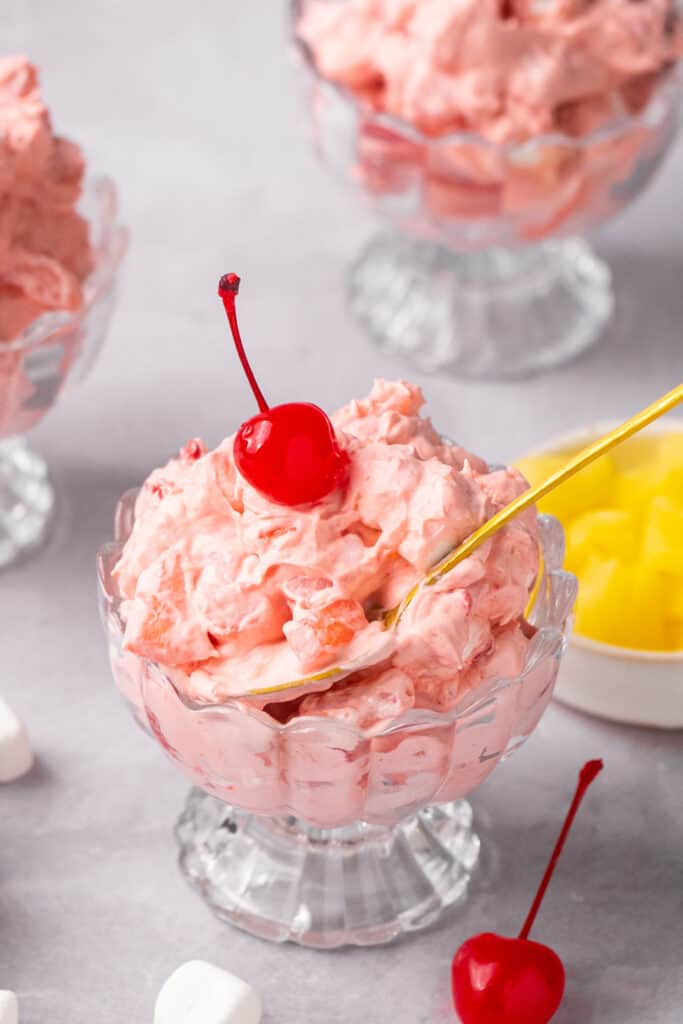 Cherry fluff recipe in a bowl topped with whipped cream and a cherry.