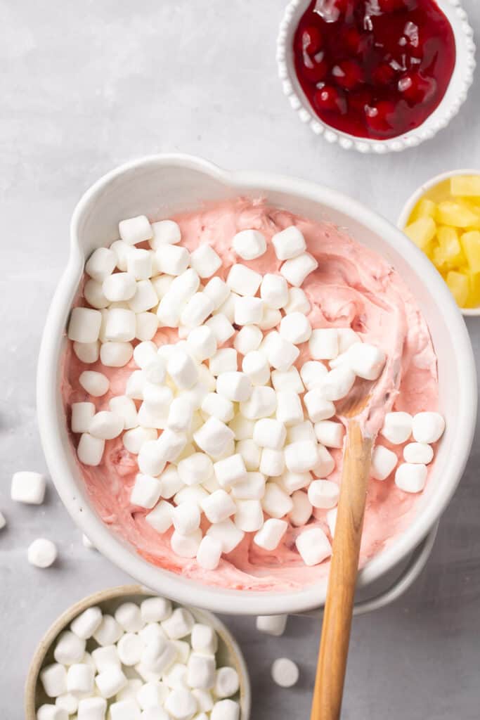 Mini marshmallows beign stirred in the cherry fluff mixture.