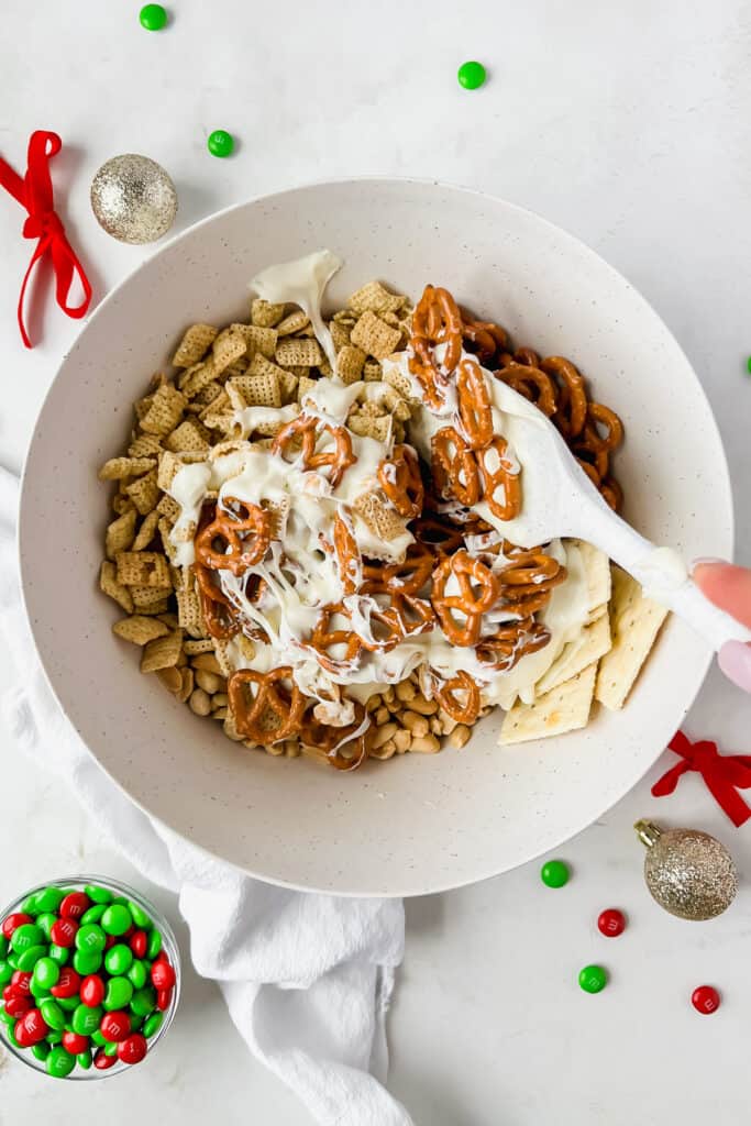 pretzels, saltines, rice chex, white chocolate being mixed together in a bowl.