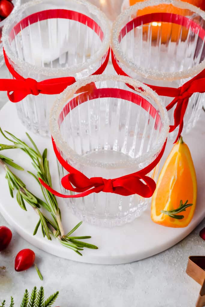 Emply glasses tied with red ribbons and garnished with rosemary, cranberry, and orange slices.