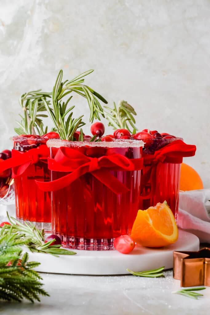 Christmas margarita recipe garnished with rosemary in short glasses tied with a red ribbon.