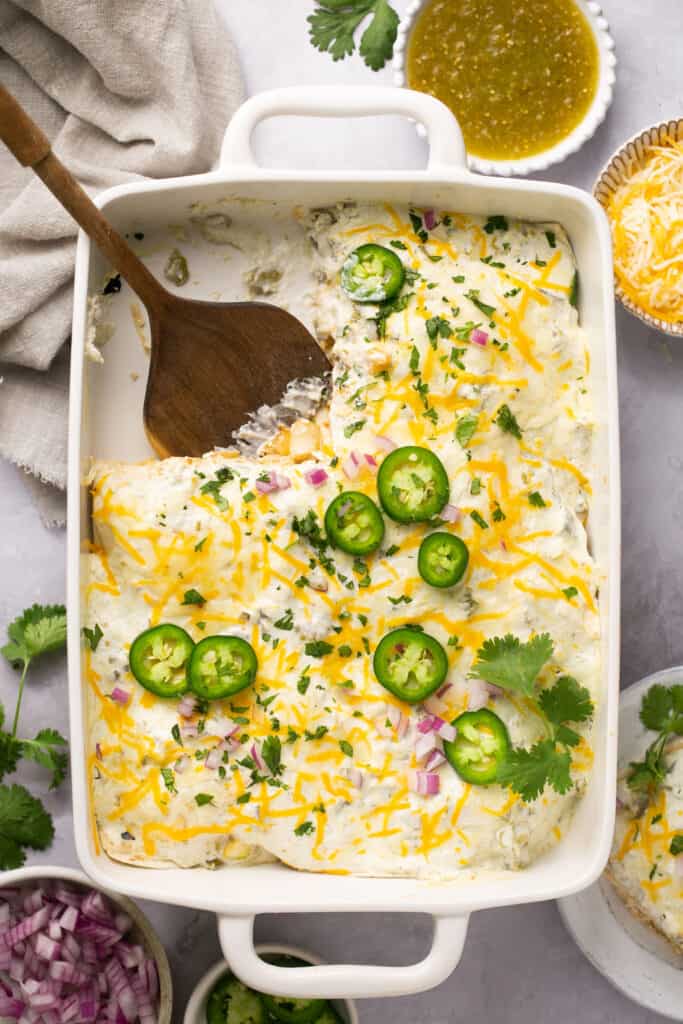 Macro Friendly Creamy Green Chili Chicken Enchilada Stack in a casserole dish with a wooden spoon