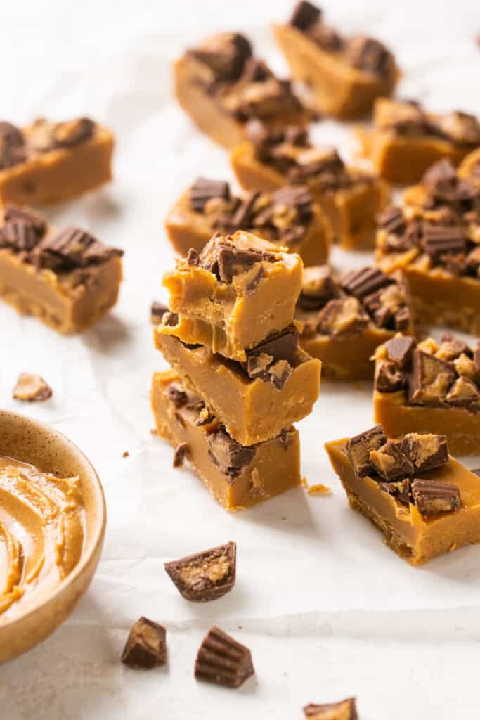 4 ingredient peanut butter fudge topped with peanut butter cups cut into bar stacked vertically