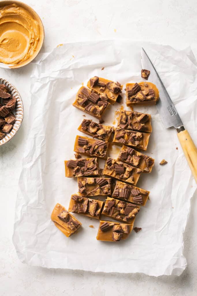 4 ingredient peanut butter fudge topped with peanut butter cups cut into bars on parchment paper.